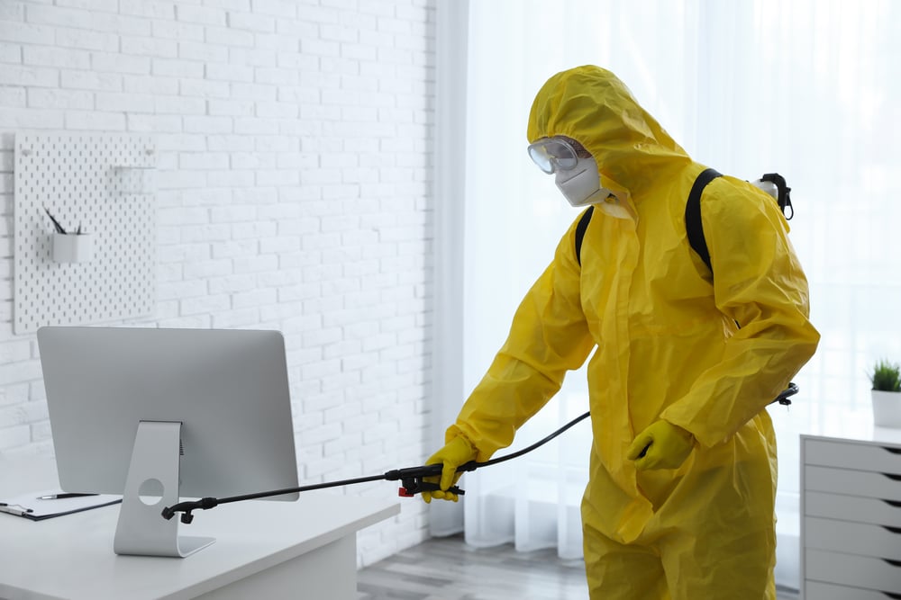 Employee in protective suit sanitizing office. Medical disinfection